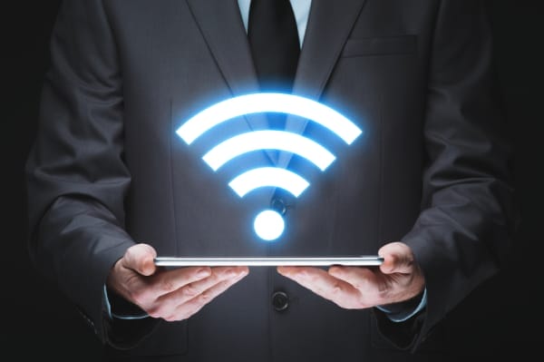 Businessman holding a tablet with a glowing Wi-Fi icon above it, symbolizing secure wireless connectivity and proactive Wi-Fi network protection.