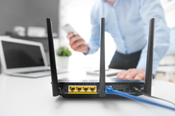 Close-up of a home Wi-Fi router with a smartphone user in the background, symbolizing the importance of securing wireless routers and configuring connectivity devices properly.