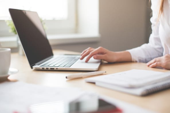 Person working at a laptop with a notebook and pen beside them, symbolizing documenting findings or preparing a recovery plan after a website hack.