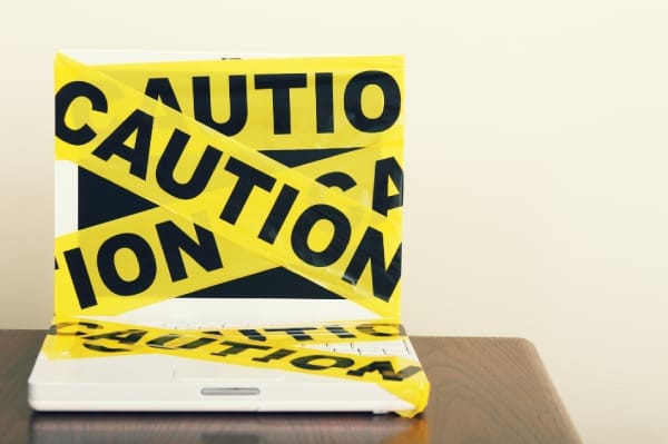 Laptop wrapped in yellow “Caution” tape, symbolizing that the website is compromised and should be handled with care.