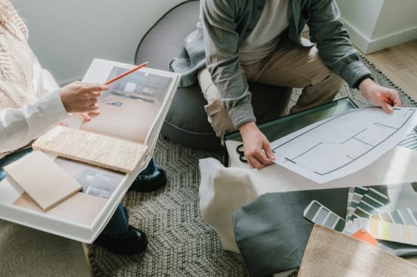 Two professionals reviewing floorplan and material samples side by side, symbolizing collaborative planning and analysis—reflecting how website recovery from a hack requires teamwork, assessment, and structured strategy.